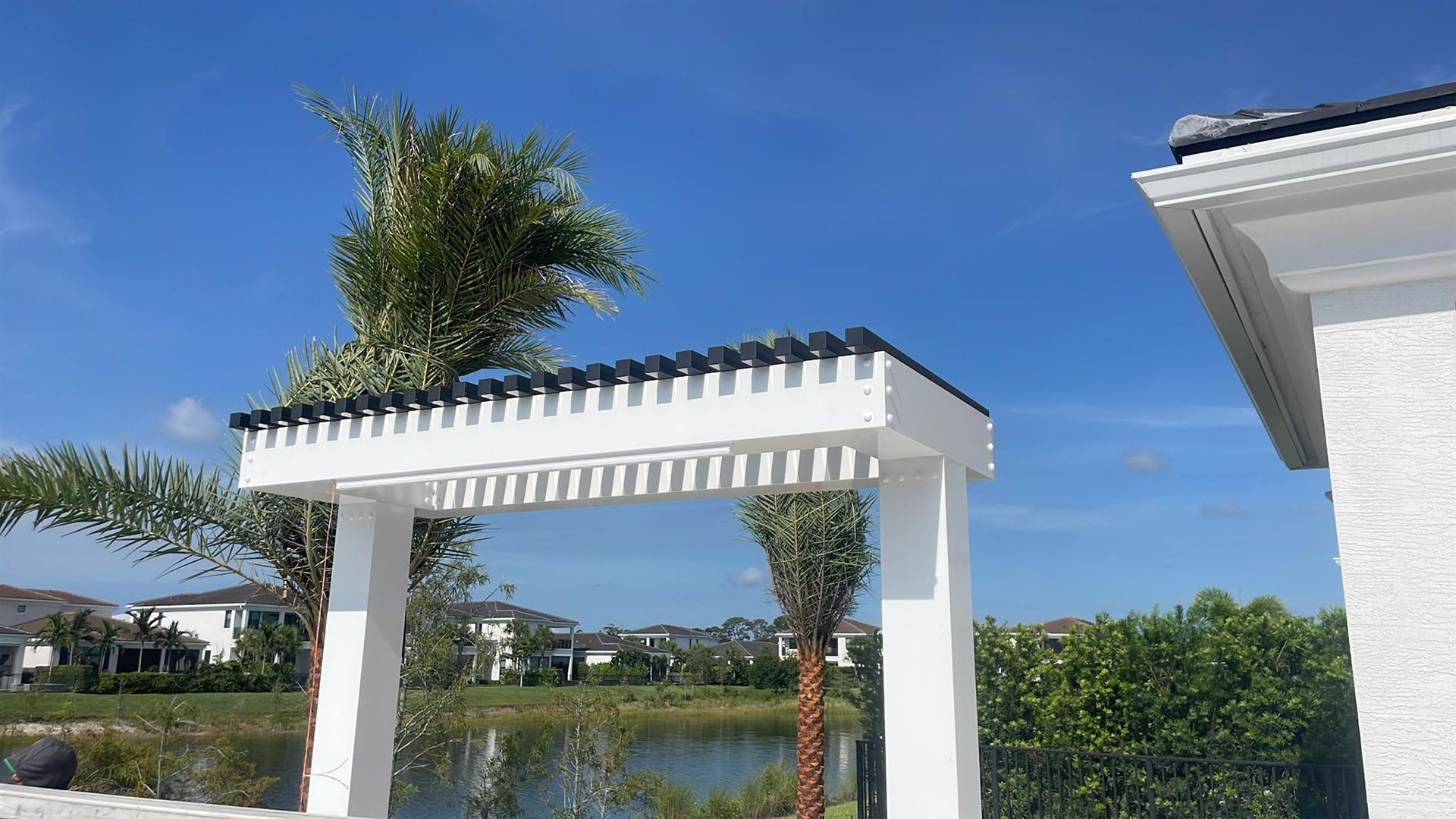 Modern white aluminum pergola with black-capped rafter tails on a lakefront lot